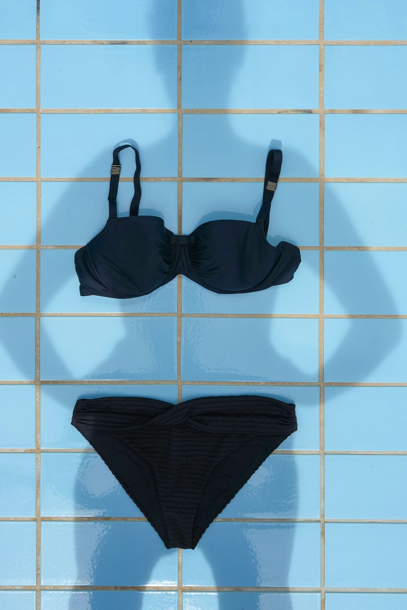 Svart bikini lagt på lyseblå bassengfliser, med skyggen av en person over